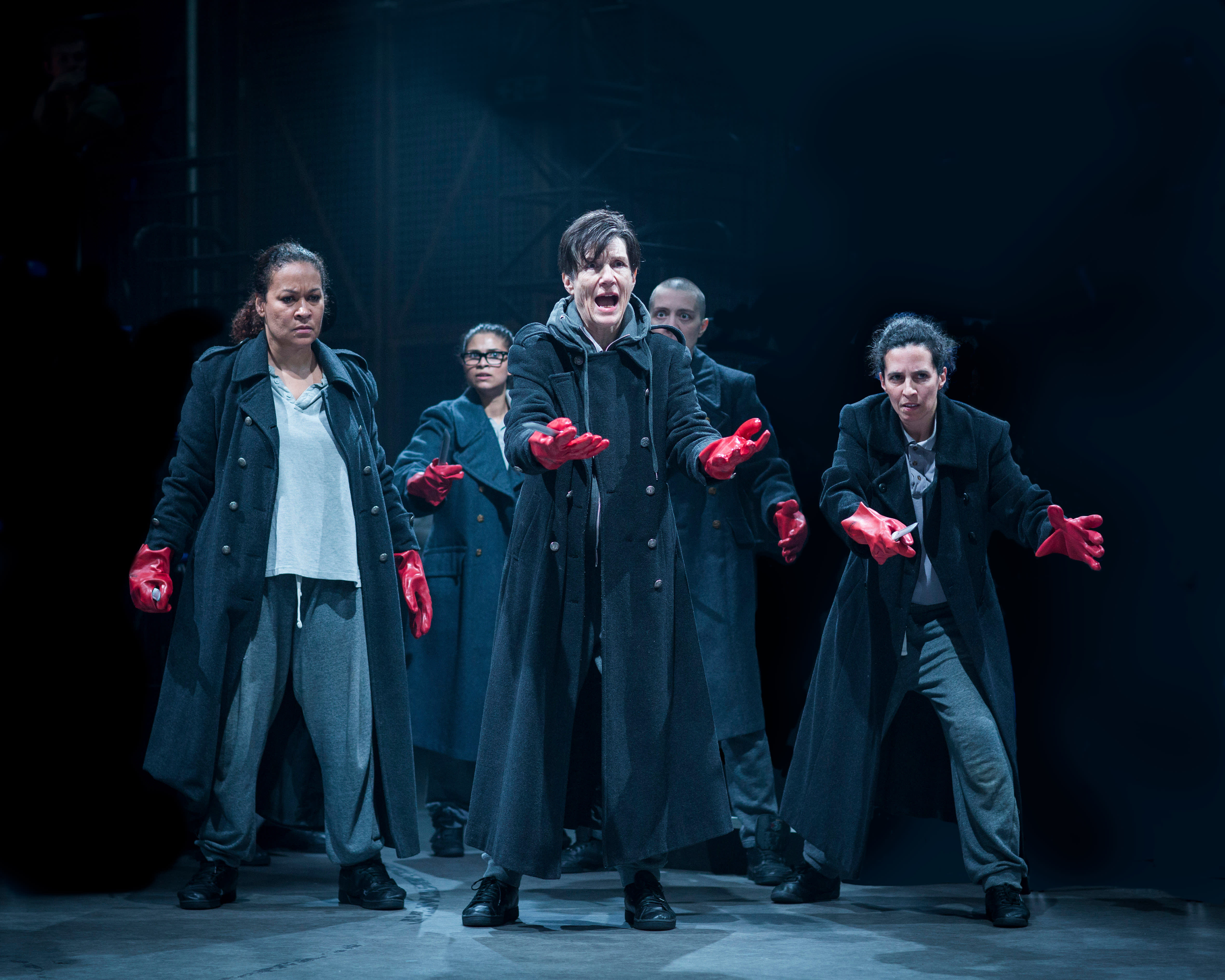 In Julius Caesar, Harriet Walter stands in front of other cast members wearing trench coats and red gloves 